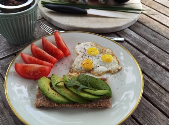 A vibrant outdoor breakfast setup with avocado toast, quail eggs, tomatoes, and tea.