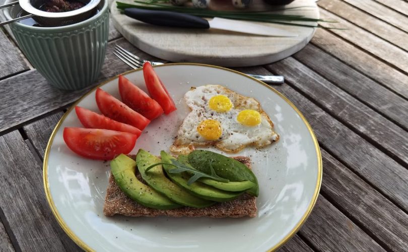 A vibrant outdoor breakfast setup with avocado toast, quail eggs, tomatoes, and tea.